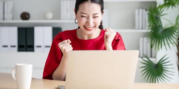 A businesswoman cheering while sitting in front of a laptop.